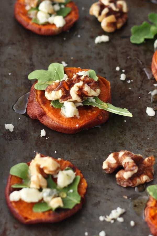 Sheet pan of sweet potato rounds topped with arugula, blue cheese, and walnuts.