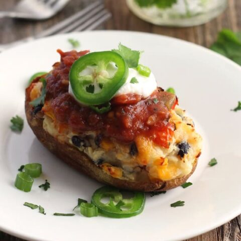 A white plate with a stuffed baked potato topped with sour cream and jalapeno slices.