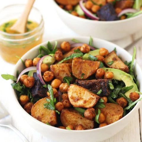 White bowls full of roasted potatoes, chickpeas, and greens on a wooden table.