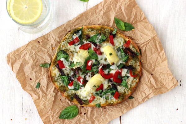 Small pizza on a piece of brown paper next to a glass of water with lemon.