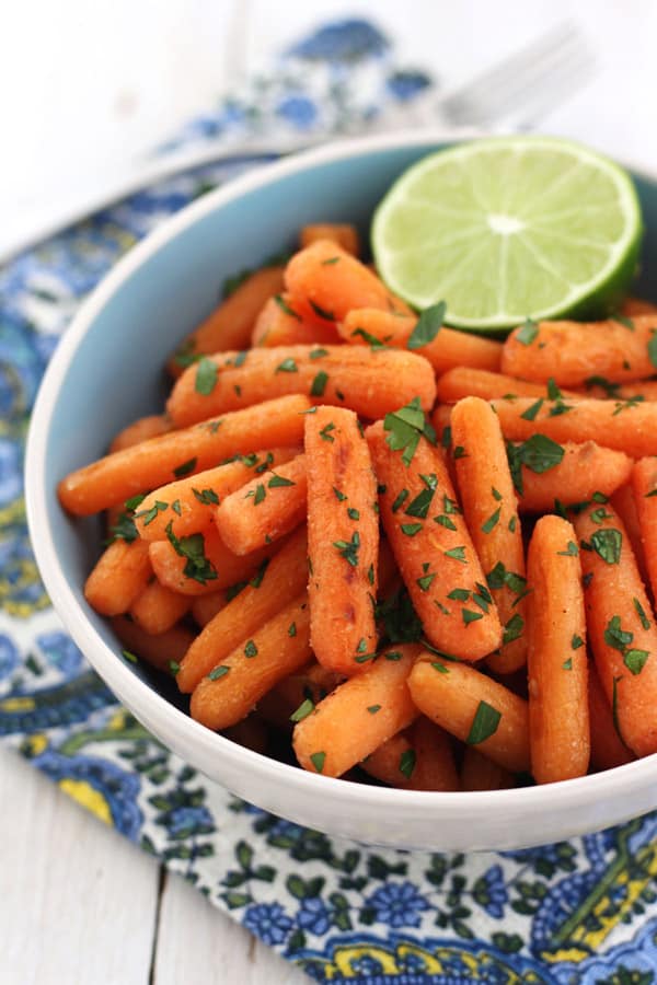 A blue bowl with roasted carrots and half a lime.