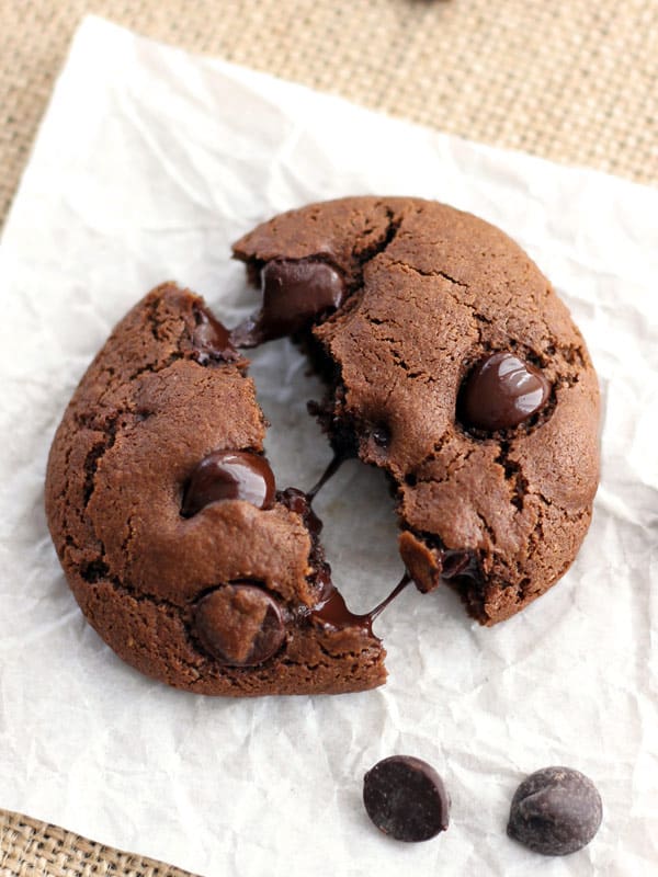 A chocolate cookie broken in half on a piece of parchment paper.