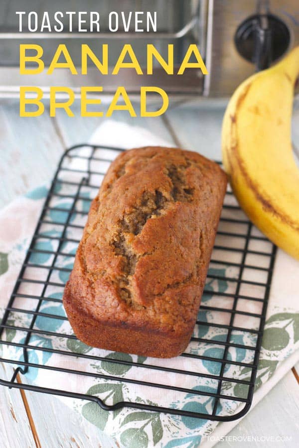 A mini loaf of banana bread cooling on a rack in front of a toaster oven