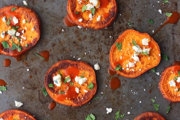 Sheet pan of roasted sweet potato slices topped with blue cheese and buffalo sauce.