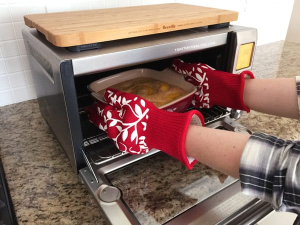 hands covered with red oven gloves reaching into a toaster oven