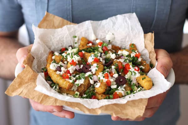 Man holding a bowl of loaded fries on parchment.