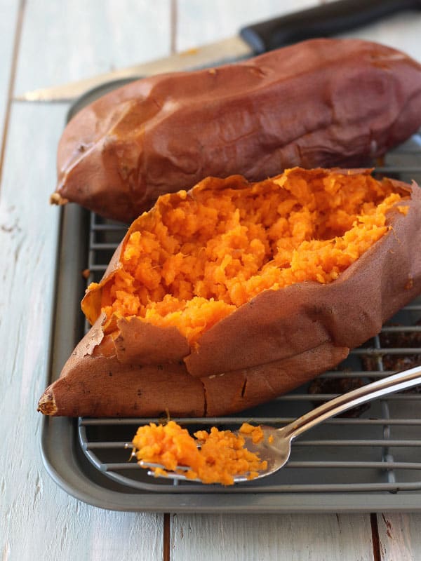 Baked sweet potato on pan sliced open with fluffy orange inside exposed