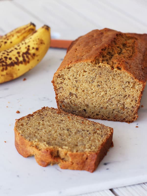 A whole loaf of banana bread sliced next to brown bananas