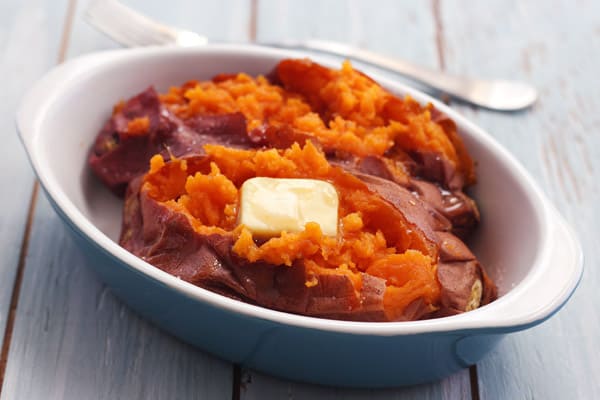 Baked sweet potato with pat of butter in a baking dish