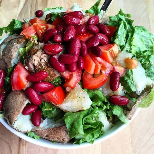 A large white bowl overflowing with lettuce, chopped baked potatoes, tomatoes, and red kidney beans.