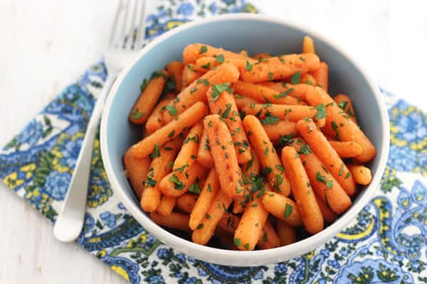 A blue bowl of carrots with a paisley napkin and fork.