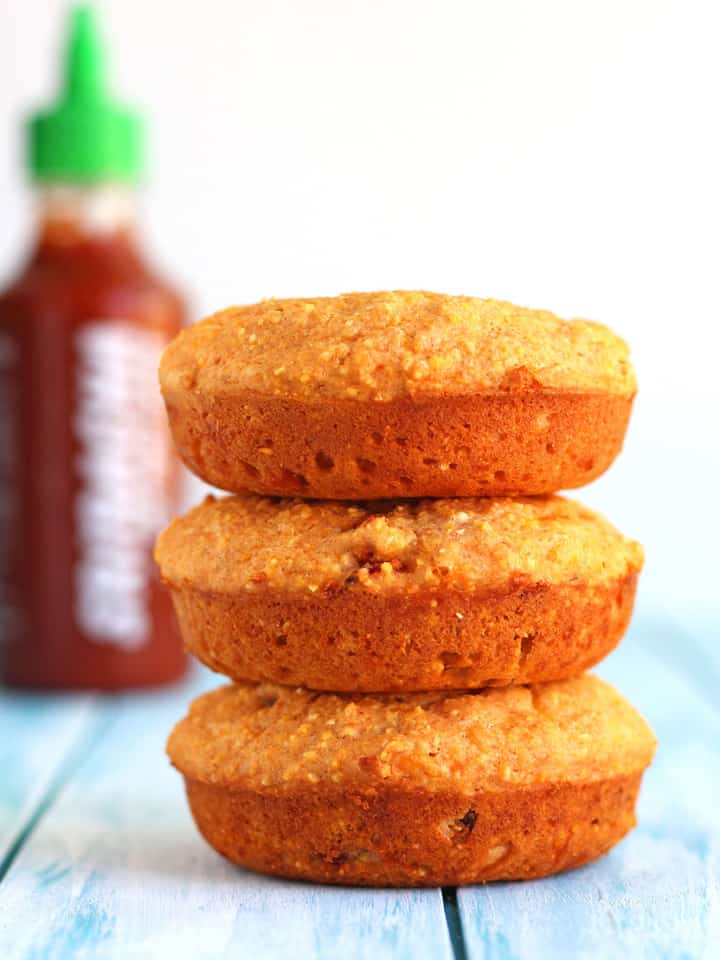 Stack of cornbread donuts next to a bottle of sriracha.