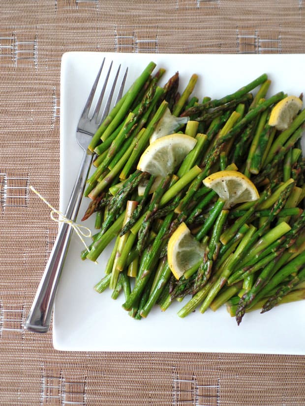 Roasted asparagus on a white plate with a fork.