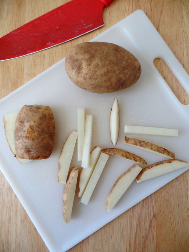 Potato sliced into sticks on a cutting board.