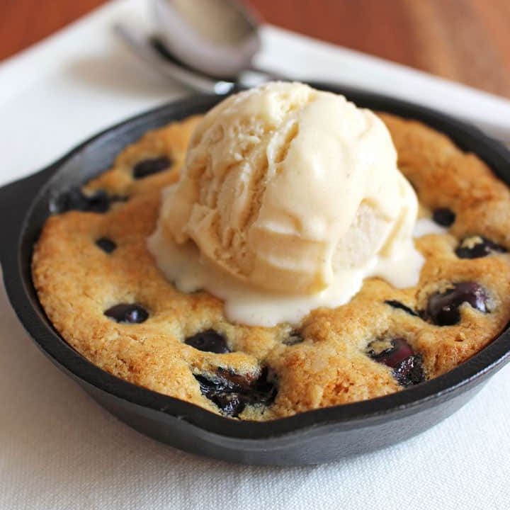 A mini skillet cookie with a scoop of ice cream melting on top on a white napkin with two spoons.