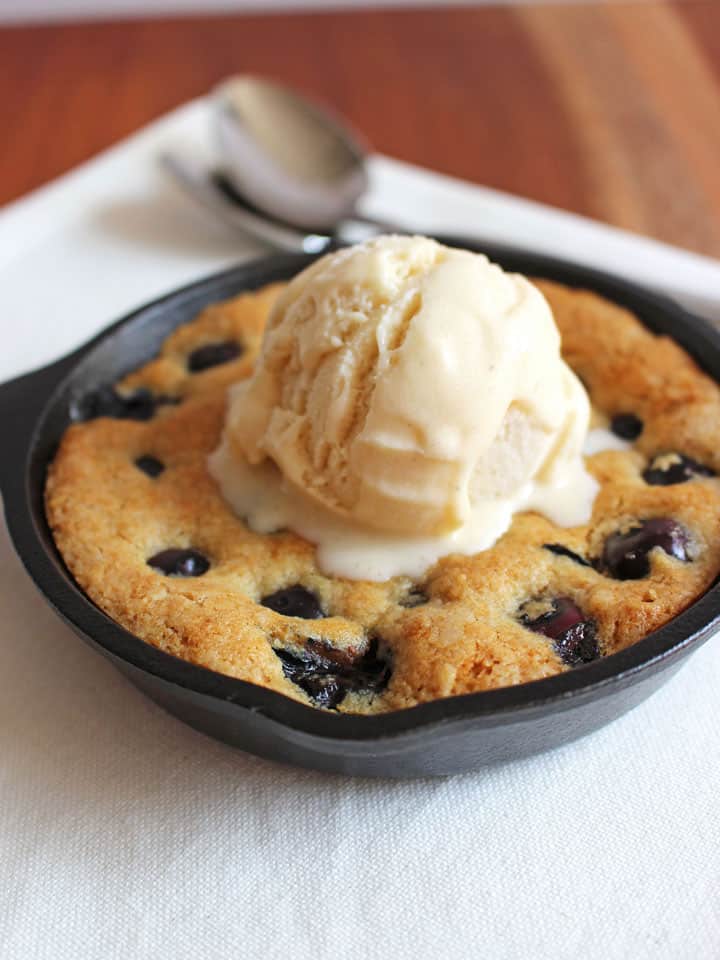 A mini skillet cookie with a scoop of ice cream melting on top on a white napkin with two spoons. 