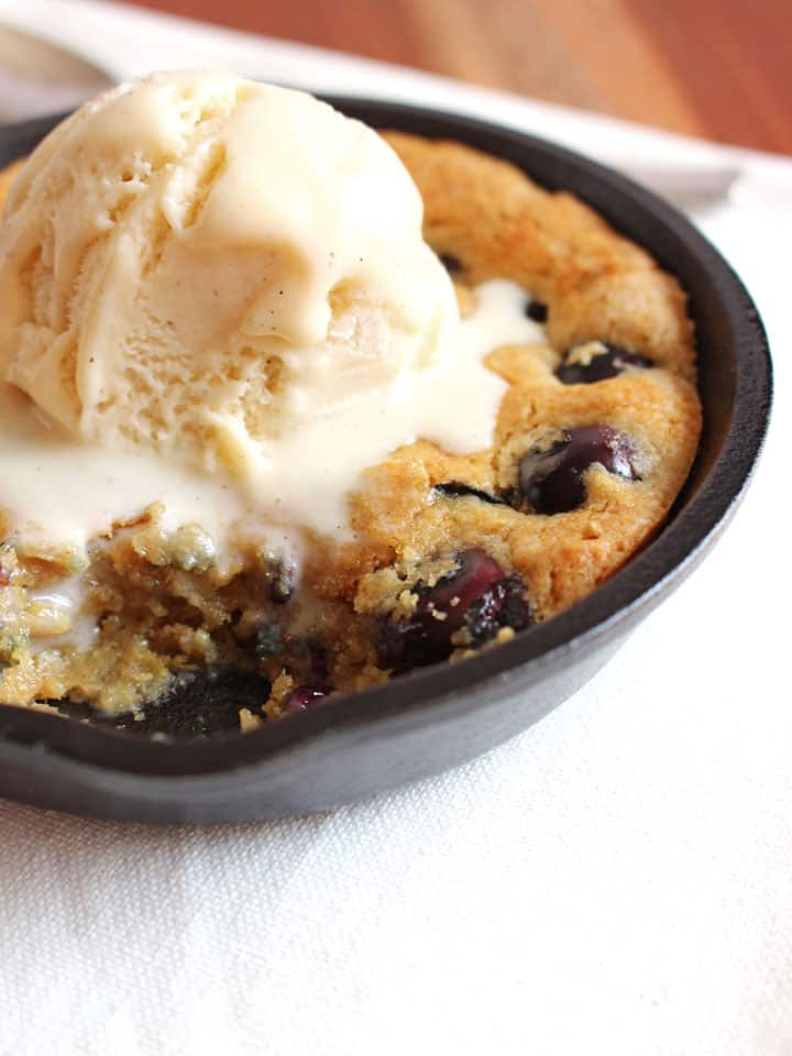 A scoop of vanilla ice cream melting inside a skillet cookie with a bite missing. 