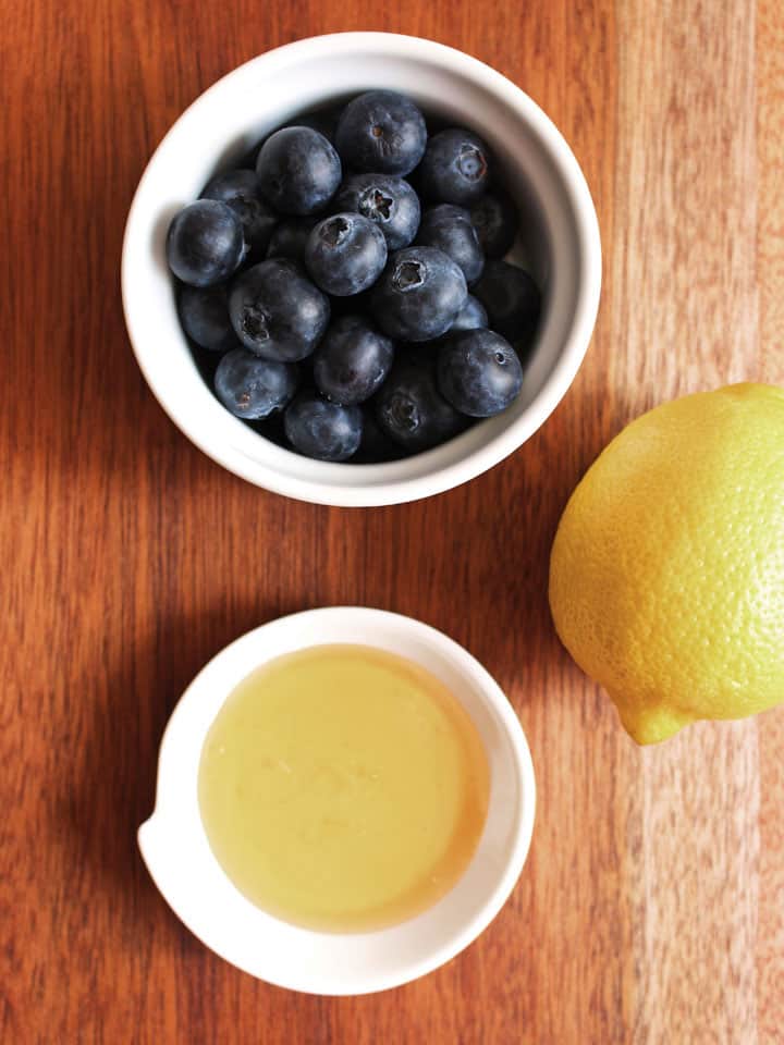 White bowls with blueberries, honey and a lemon a wooden table.