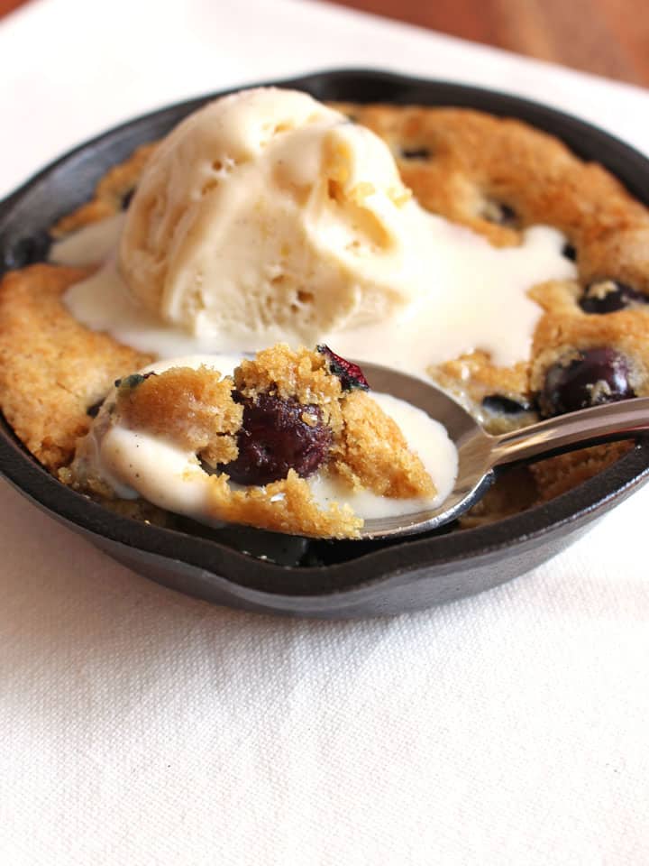 A spoon filled with cookie and melting ice cream resting on a mini skillet.