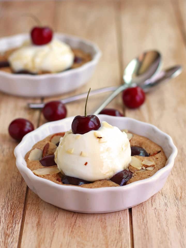 Mini dish of baked cherry cake with a scoop of yogurt and a fresh cherry.