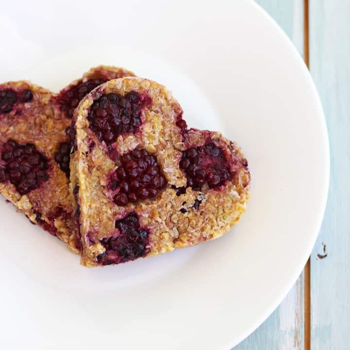 Two heart-shaped oat cookies with blackberries.