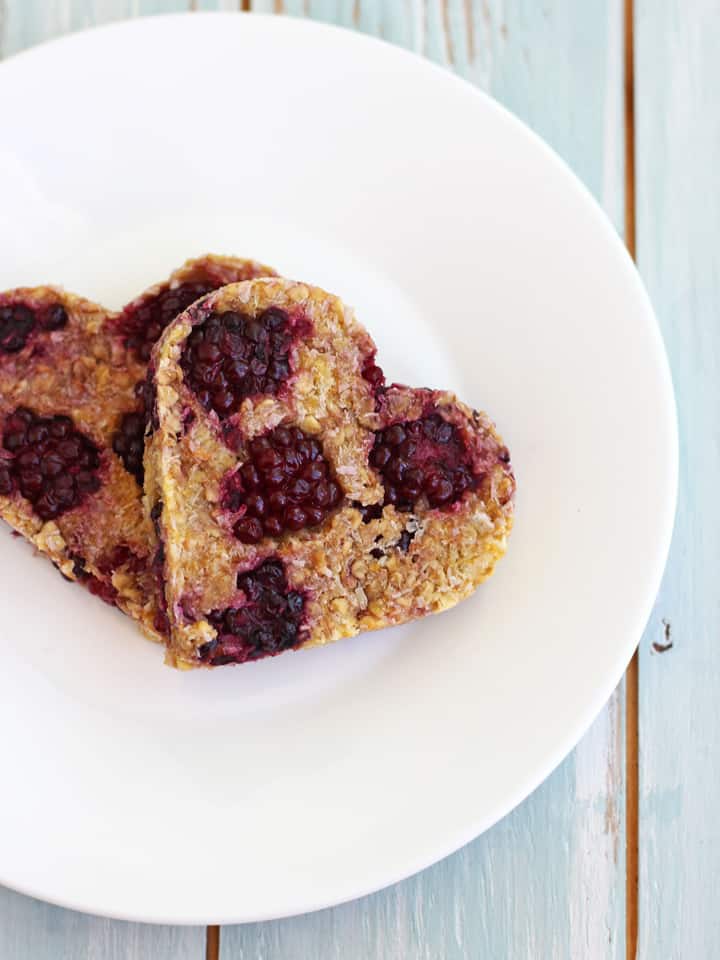 Two heart-shaped oat cookies with blackberries.