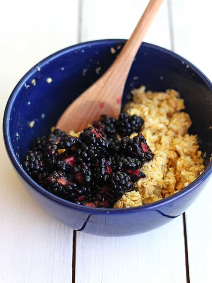 Wooden spoon stirring chopped blackberries into an oat mixture.