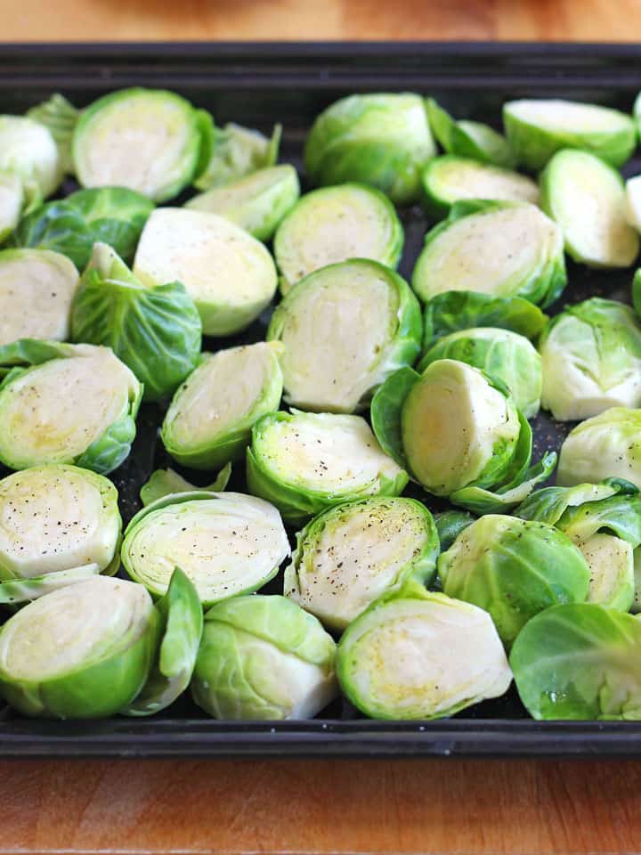 Brussels sprouts halves on a dark roasting pan.