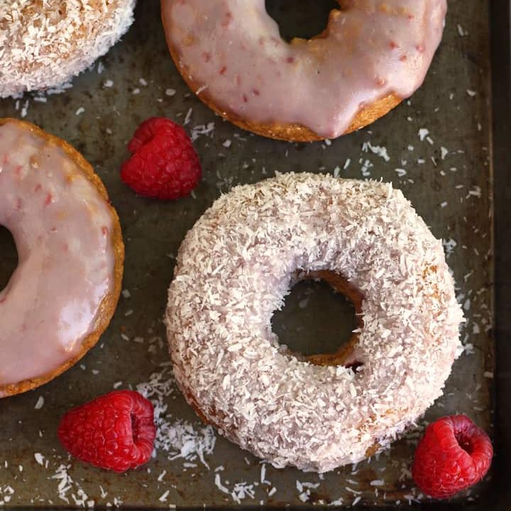 Baked donuts and fresh raspberries on a metal baking sheet.