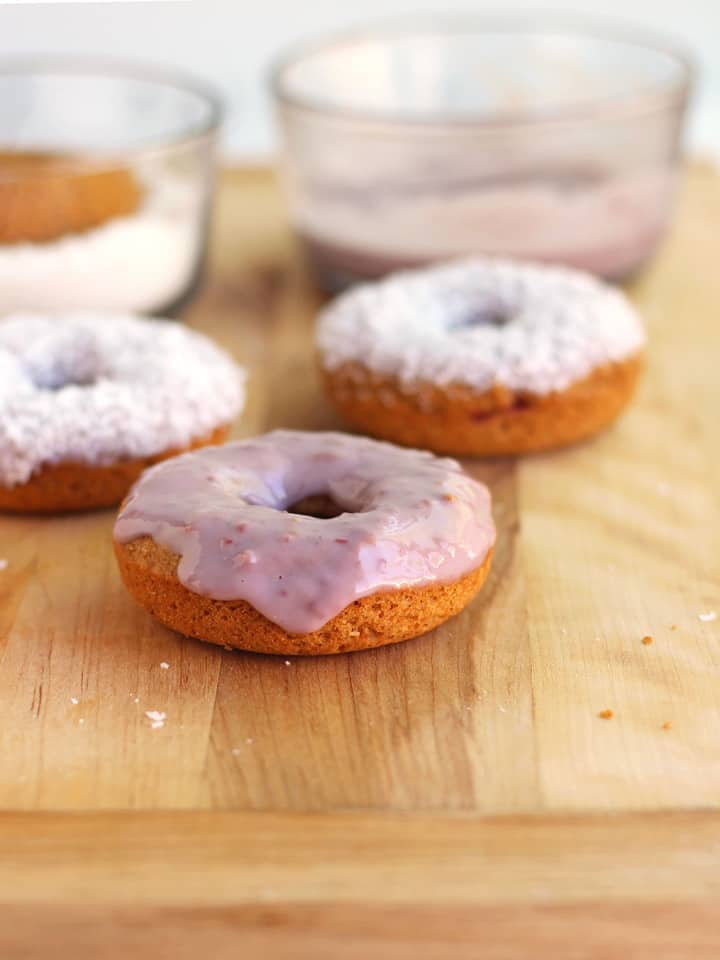 Donuts with raspberry glaze on a wooden cutting board.