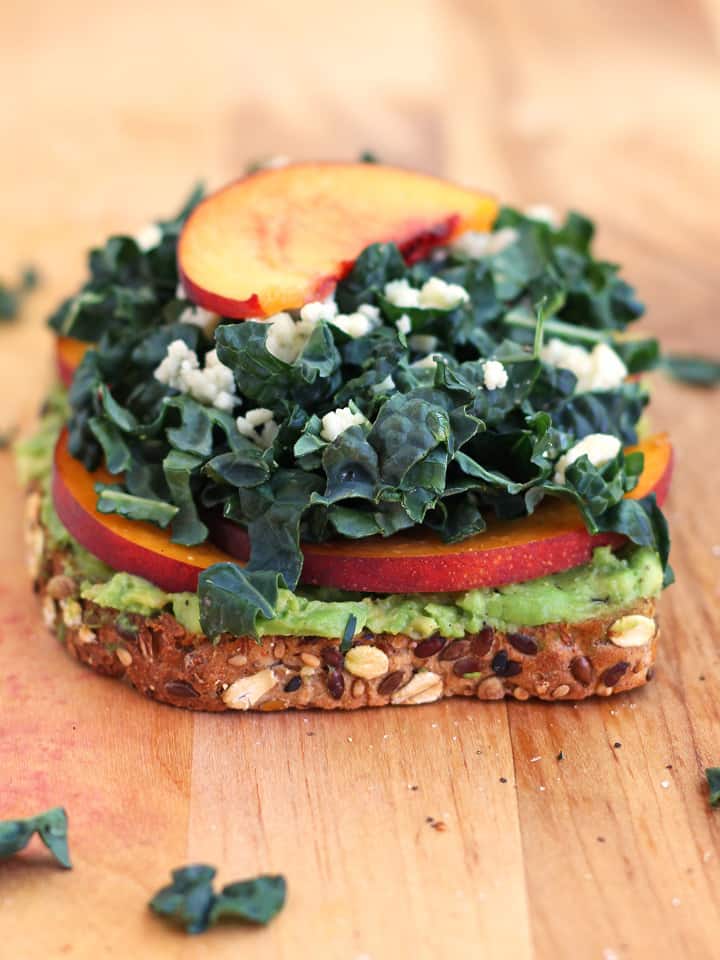 Side view of toast showing layers of avocado, peach slices, and kale.