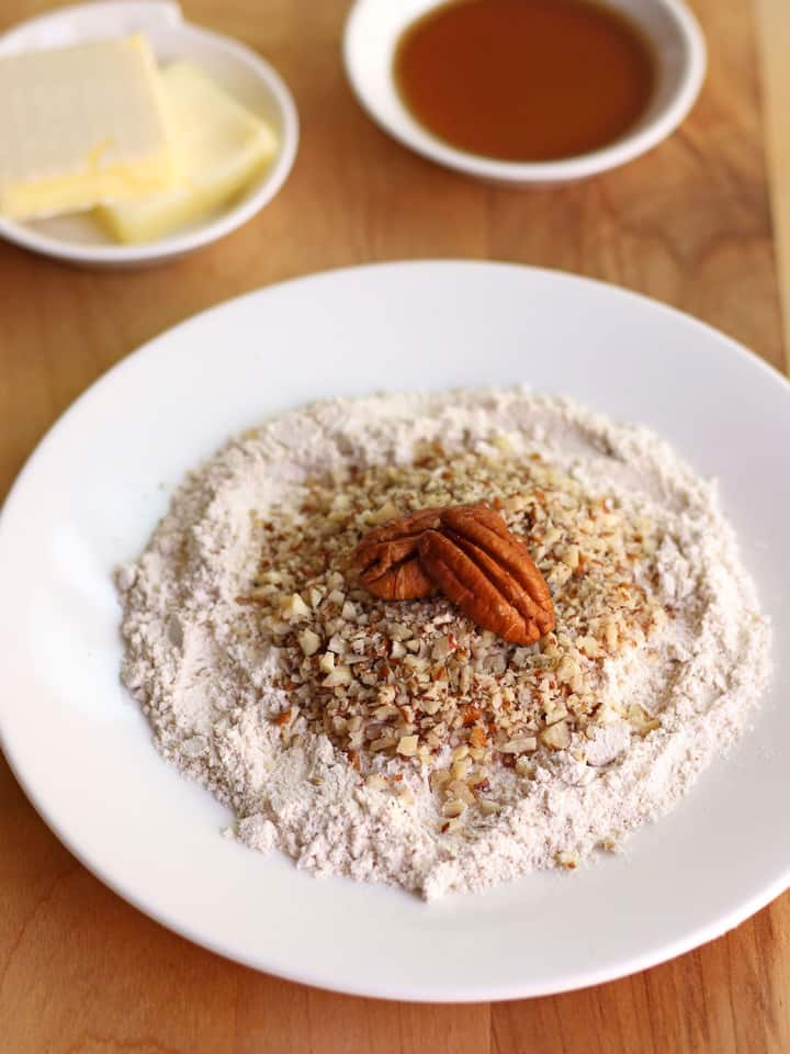 Flour and chopped nuts on a plate next to butter and maple syrup.