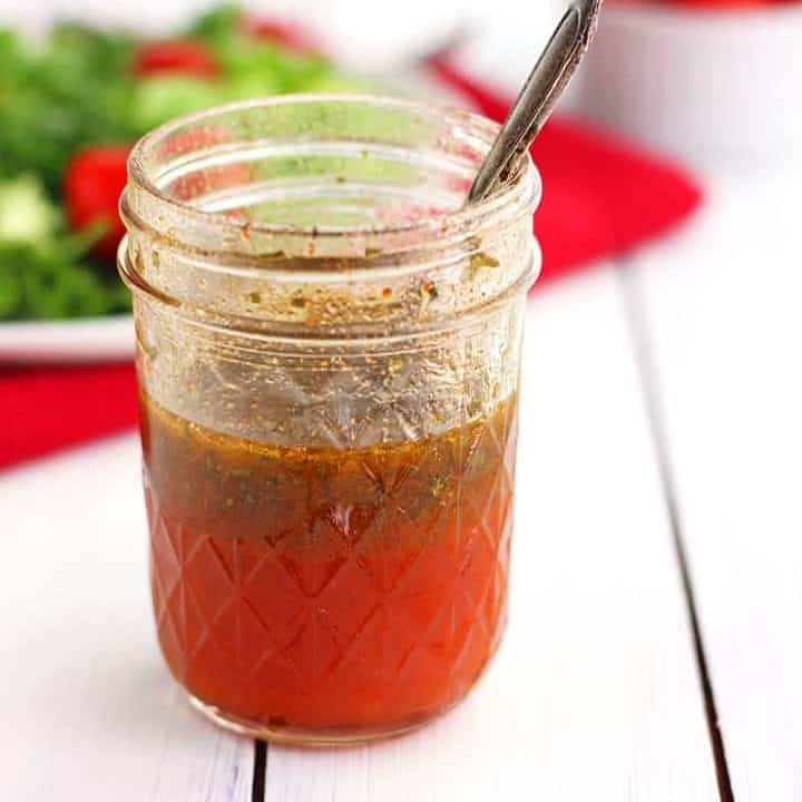 Glass jar of red salad dressing on a white table.