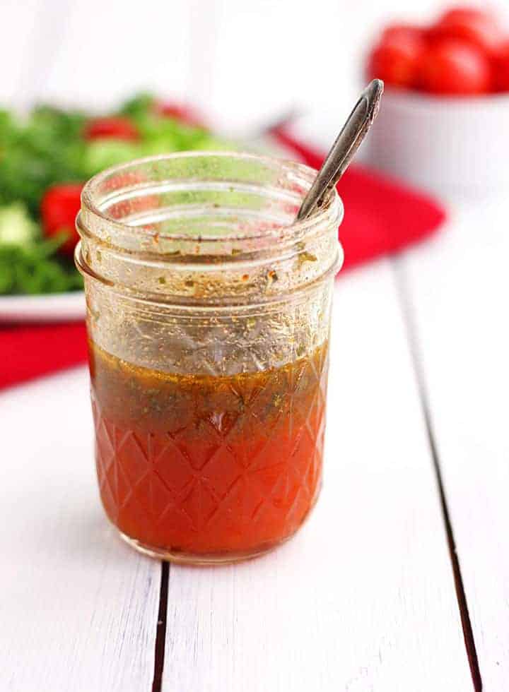 Glass jar of red salad dressing on a white table.