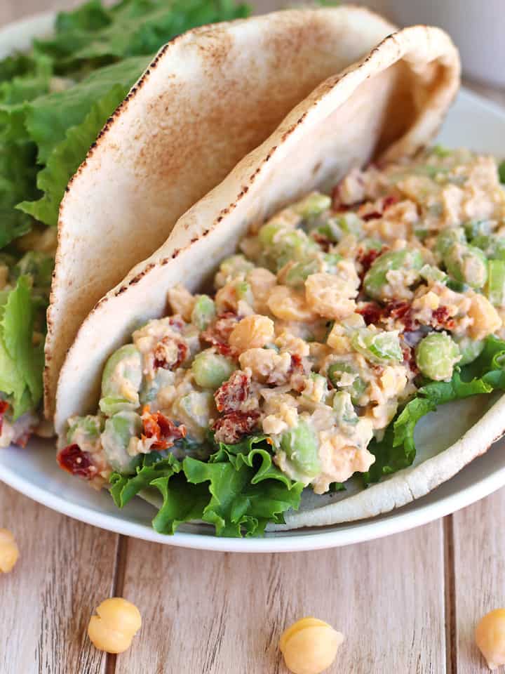 Filled pitas on a white plate on a wooden table with loose chickpeas.