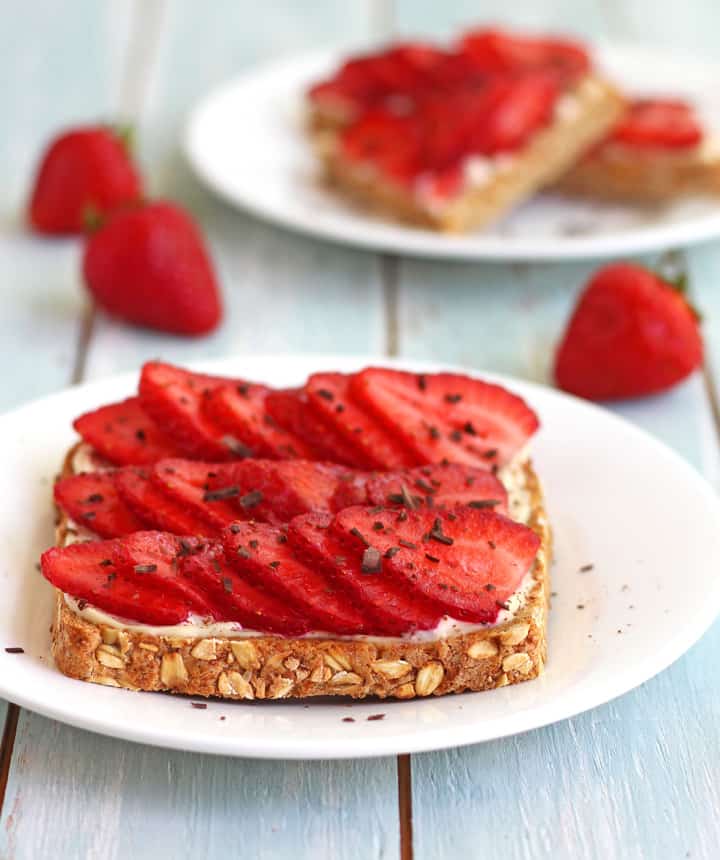 Toasts on white plates with fresh strawberries.