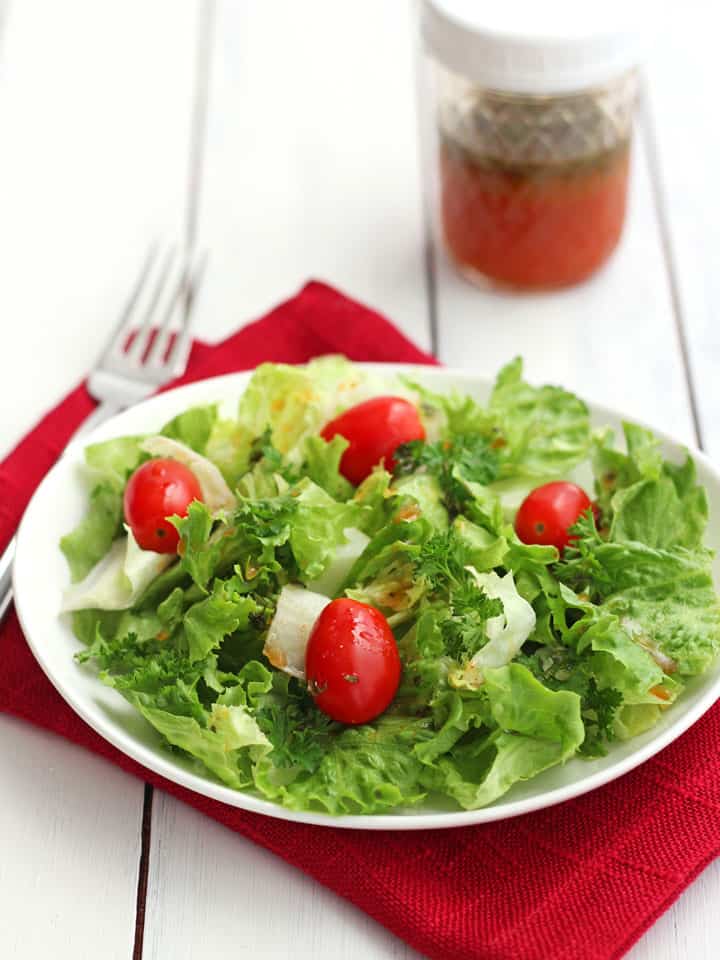 Small green salad with grape tomatoes next to a jar of dressing.