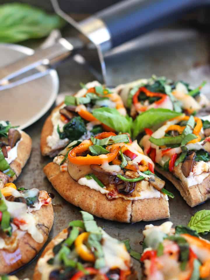 Mini pizza bites on a sheet pan with a pizza cutter.