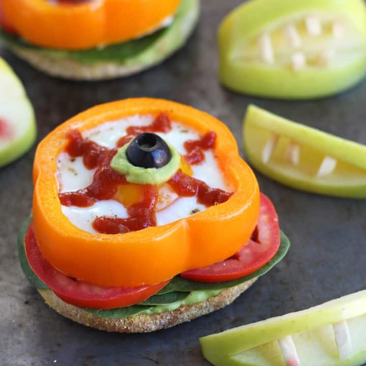 Eggs baked in orange bell pepper slices next to apples with almond 'vampire' teeth.