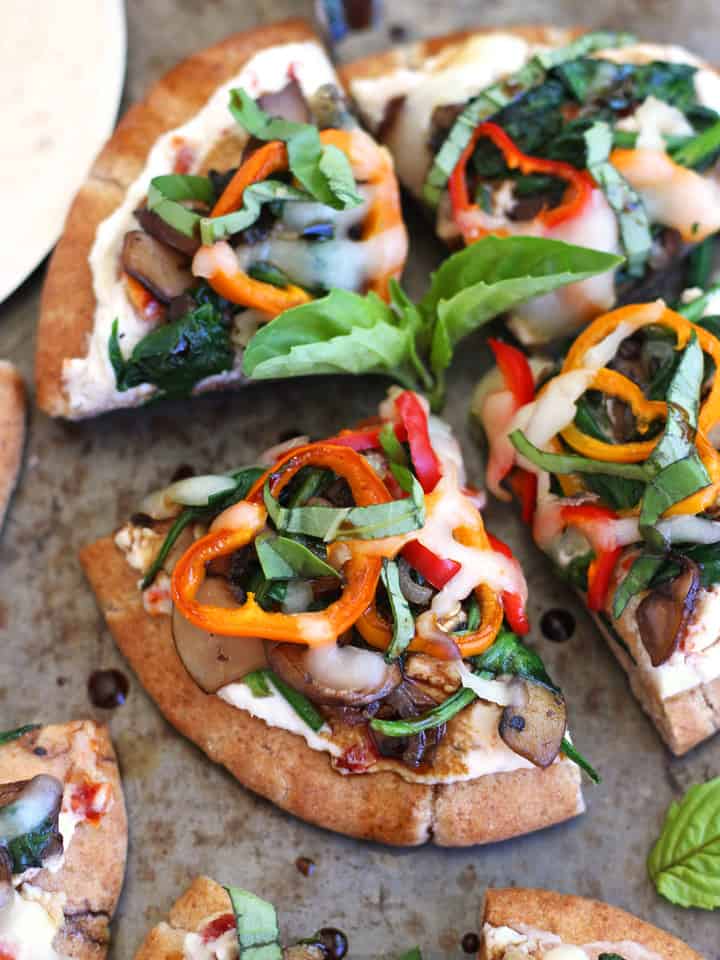 Close up of a slice of mini pita topped with veggies and fresh basil.