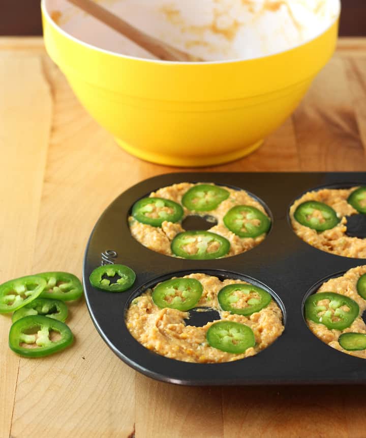 Batter spooned into a donut pan and topped with jalapeno slices.