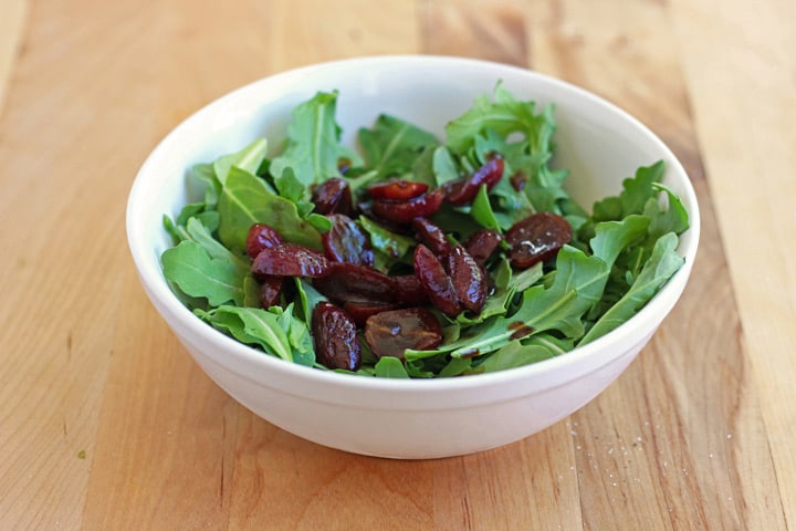 White bowl with arugula and balsamic roasted grapes.