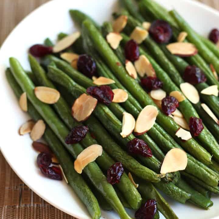 A plate of green beans topped with dried cranberries and toasted almond slices.