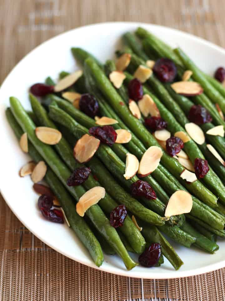 A plate of green beans topped with dried cranberries and toasted almond slices.