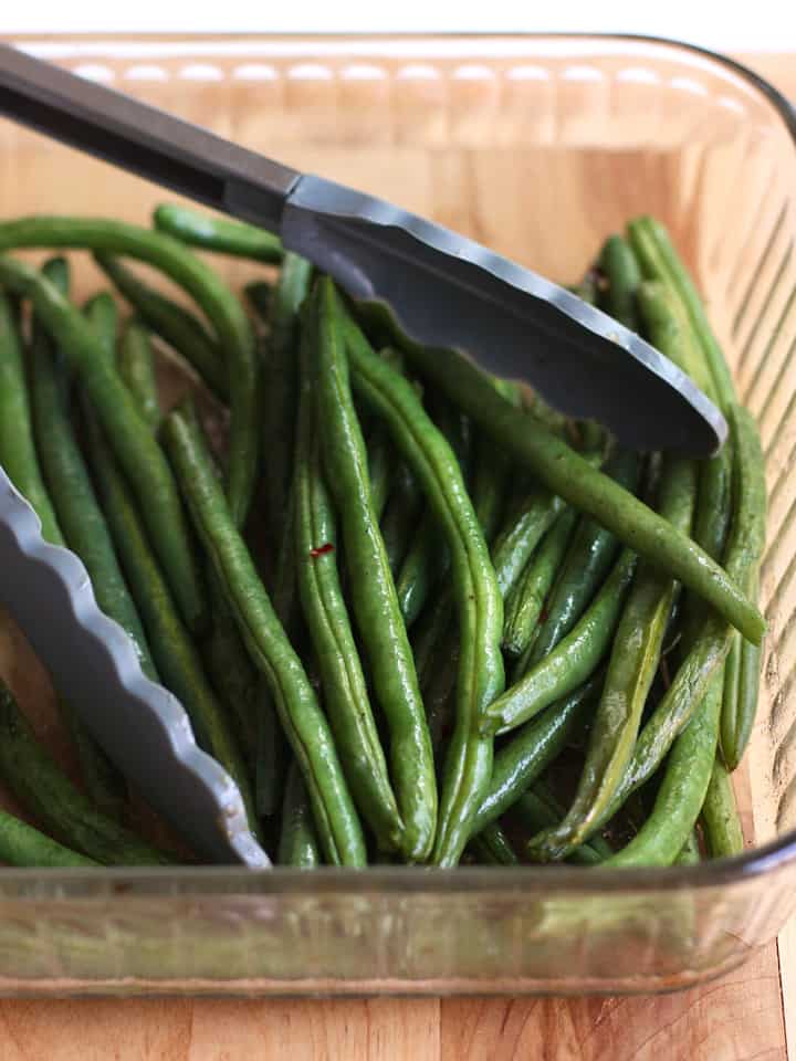 Roasted Green Beans in a glass baking dish with a pair of tongs.