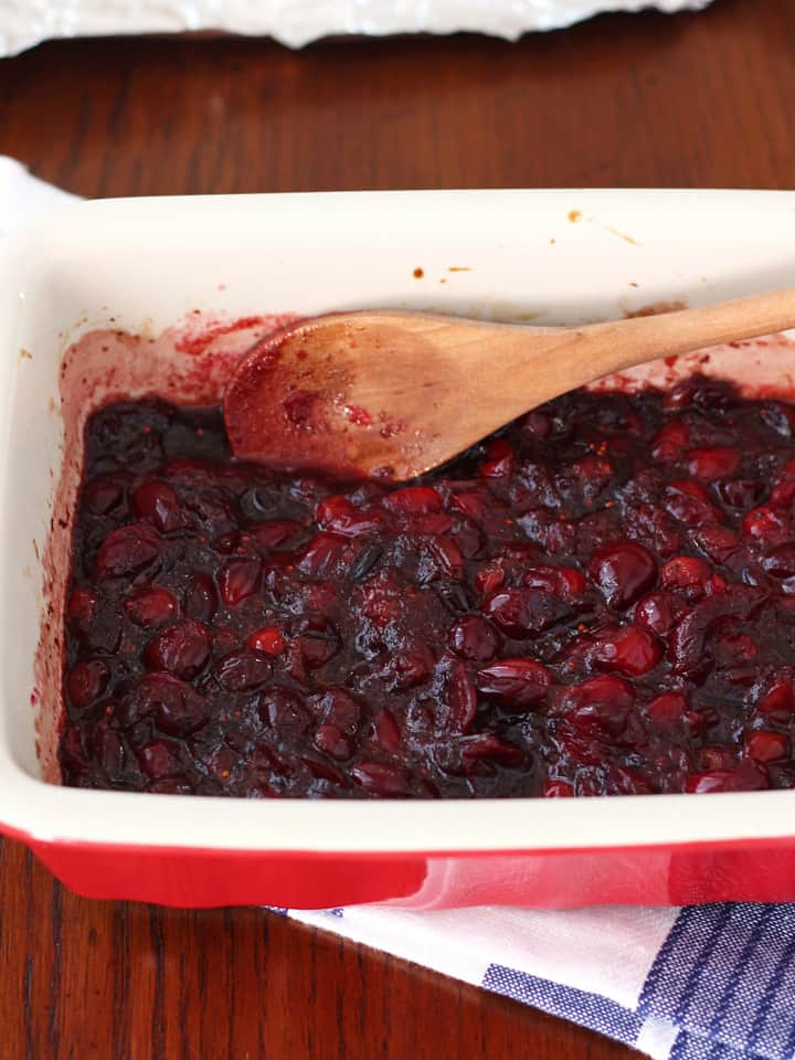 Wooden spoon stirring balsamic roasted cranberries in a baking dish.