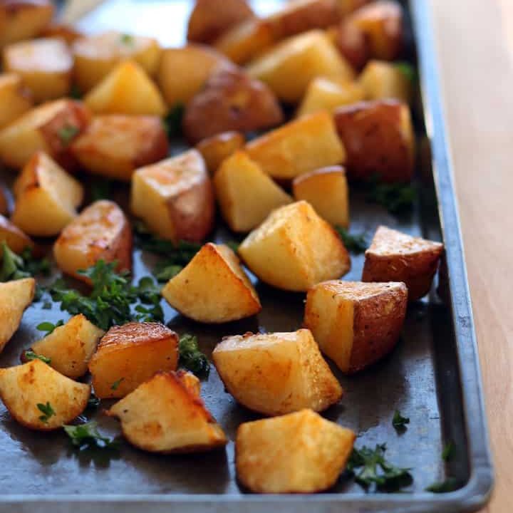 Roasted potato cubes on a dark sheet pan.