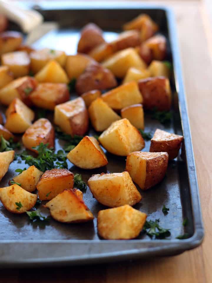 Roasted potato cubes on a sheet pan with a spatula.