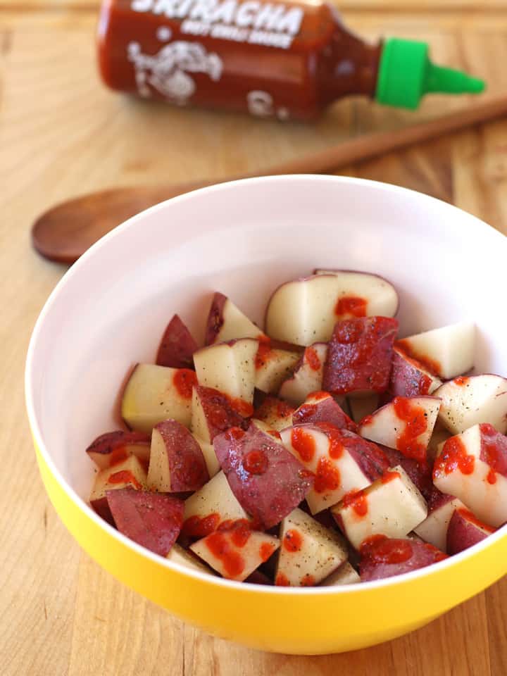 A yellow bowl with potato cubes drizzled with sriracha sauce.