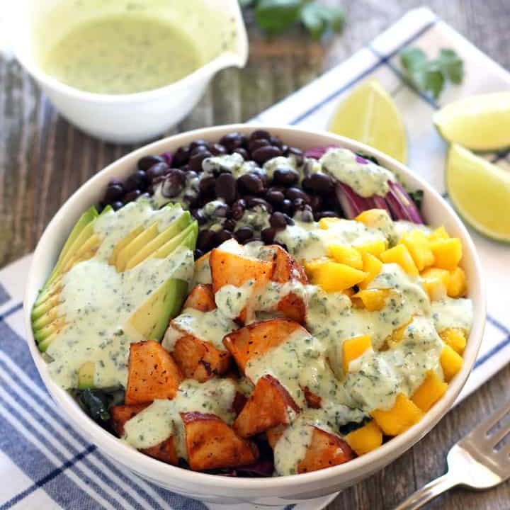 A white bowl with salad next to a cup of dressing.